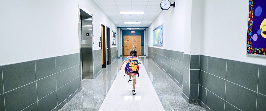 young boy running down school hallway with backpack