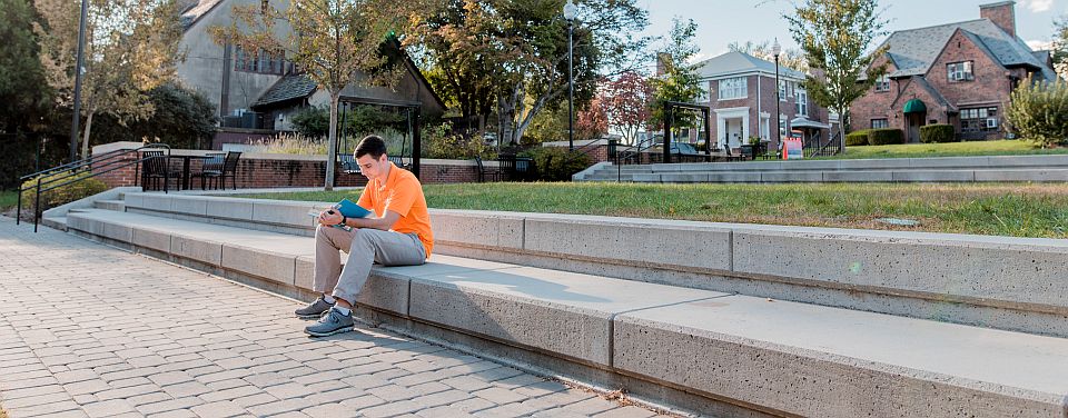male student sitting outside studying on campus